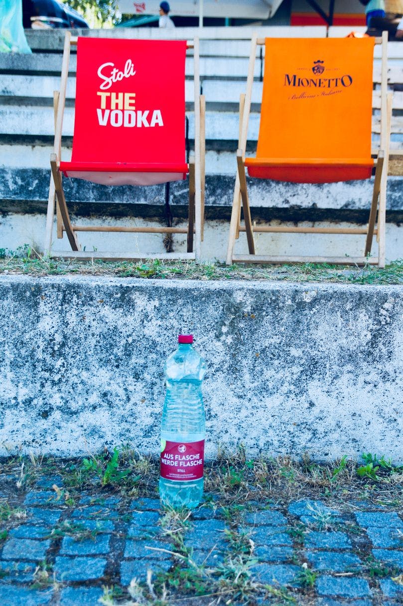 Zwei Liegestühle, gebrandet von Stolinchnaya Vodka und Mionetto, auf der Tribüne. Im Vordergrund eine Mineralwasserflasche.